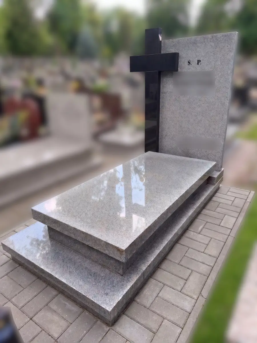 Nagrobek z szarego granitu z pełną płytą, stelą i czarnym krzyżem, na opasce z kostki brukowej