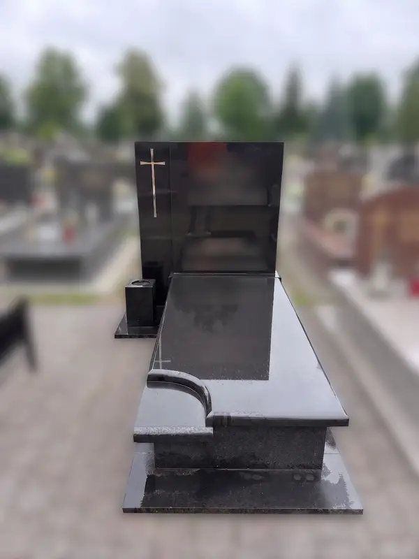 Nagrobek z czarnego polerowanego granitu ze złotym krzyżem na steli, na cmentarzu