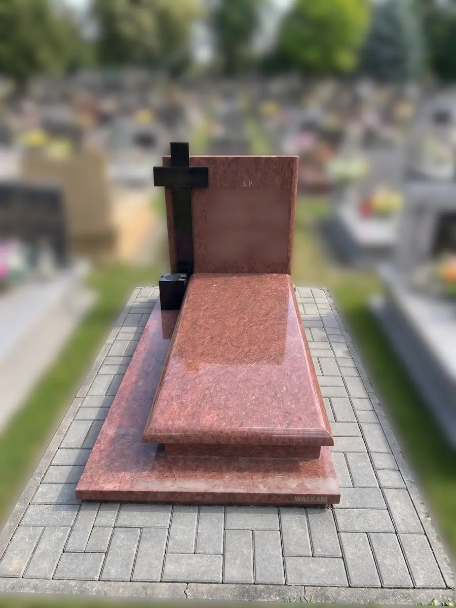 Nagrobek z czerwonego granitu z czarnym krzyżem na opasce z szarej kostki brukowej