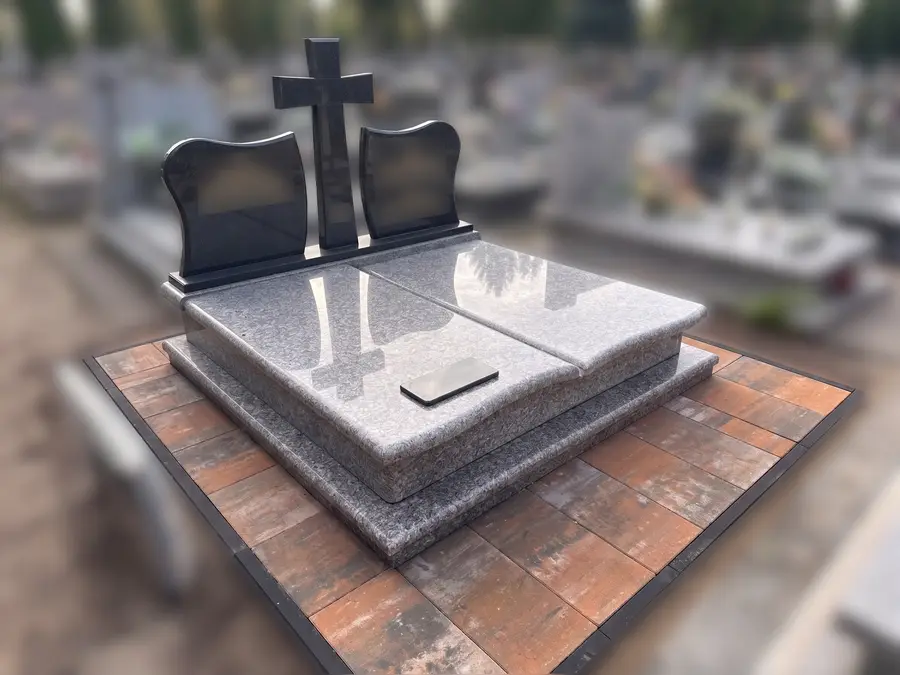 Pomnik rodzinny podwójny z dwiema płytami z szarego granitu, krzyżem pośrodku i dwiema czarnymi stelami, na opasce z czerwonej kostki brukowej